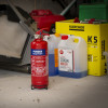 Red ultrafire 2kg powder fire extinguisher standing on workshop floor with other equipment behind it